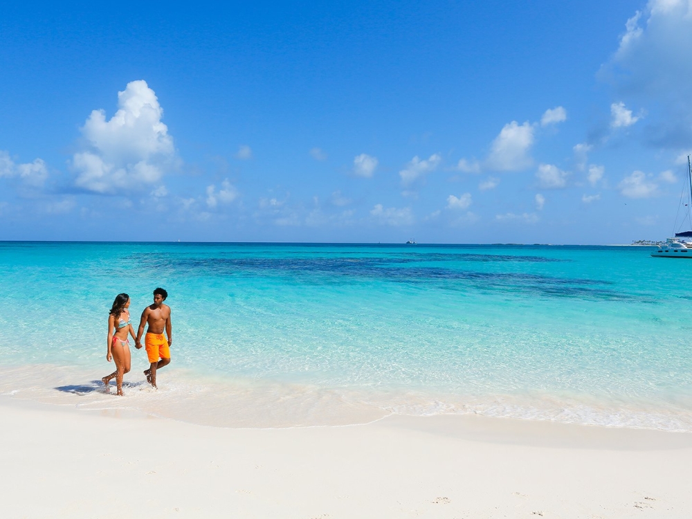 A man and woman walk hand-in-hand down a white sand beach.